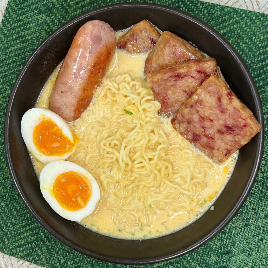 Un cuenco de ramen cremoso con lonchas de Spam, una salchicha entera y dos mitades de huevo con la yema líquida.