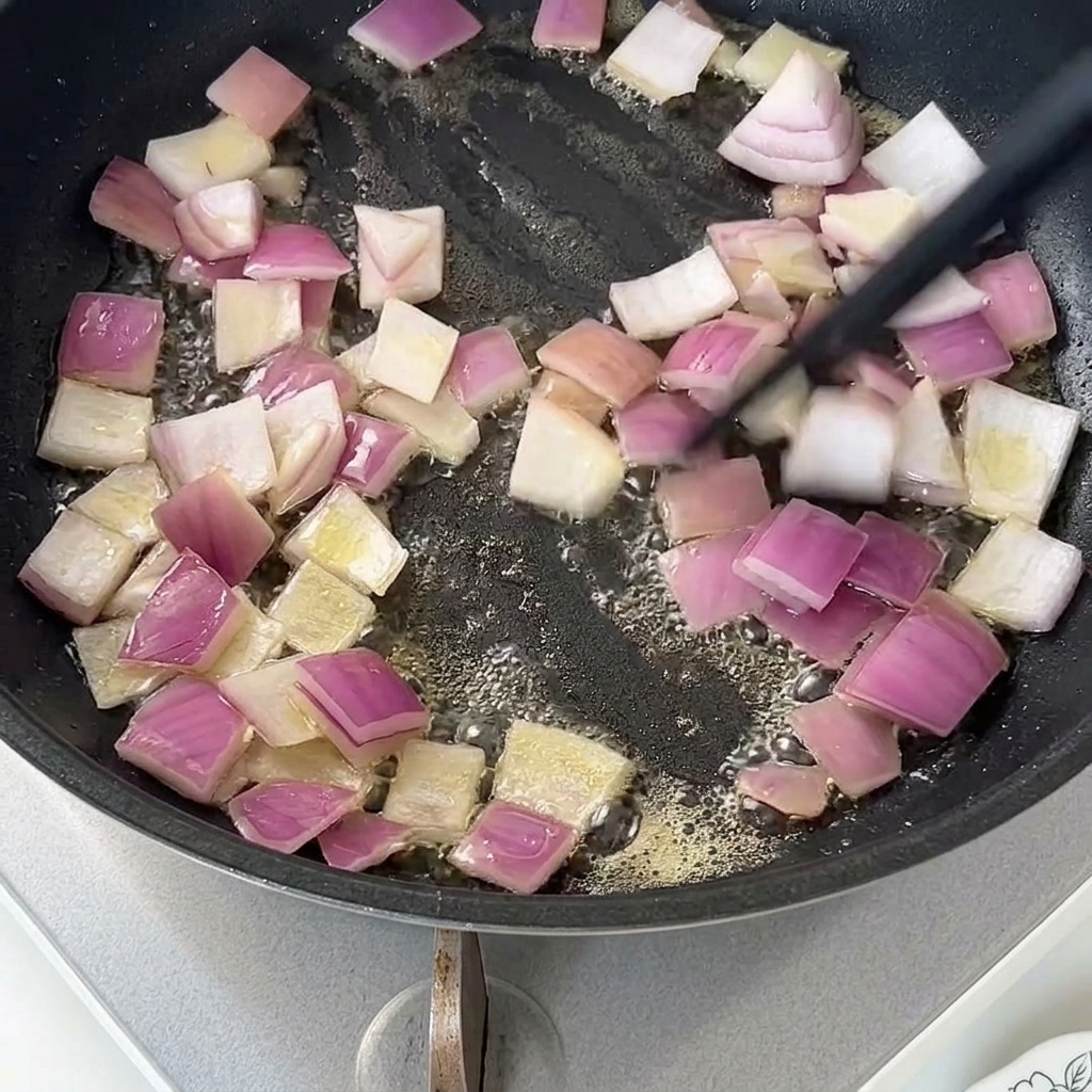 Cebolla roja picada sofriéndose en mantequilla derretida en una sartén antiadherente.