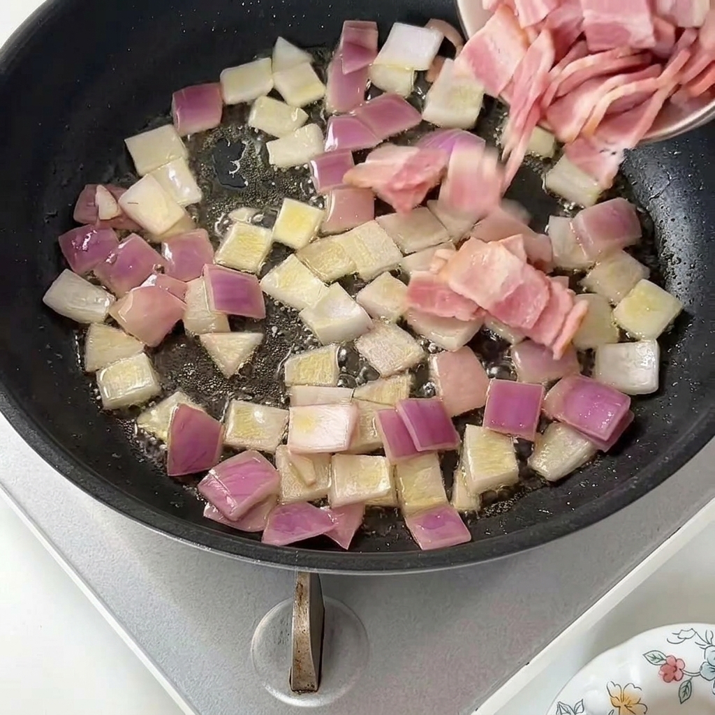 Añadiendo trozos de beicon crudo a la sartén con la cebolla roja sofrita.