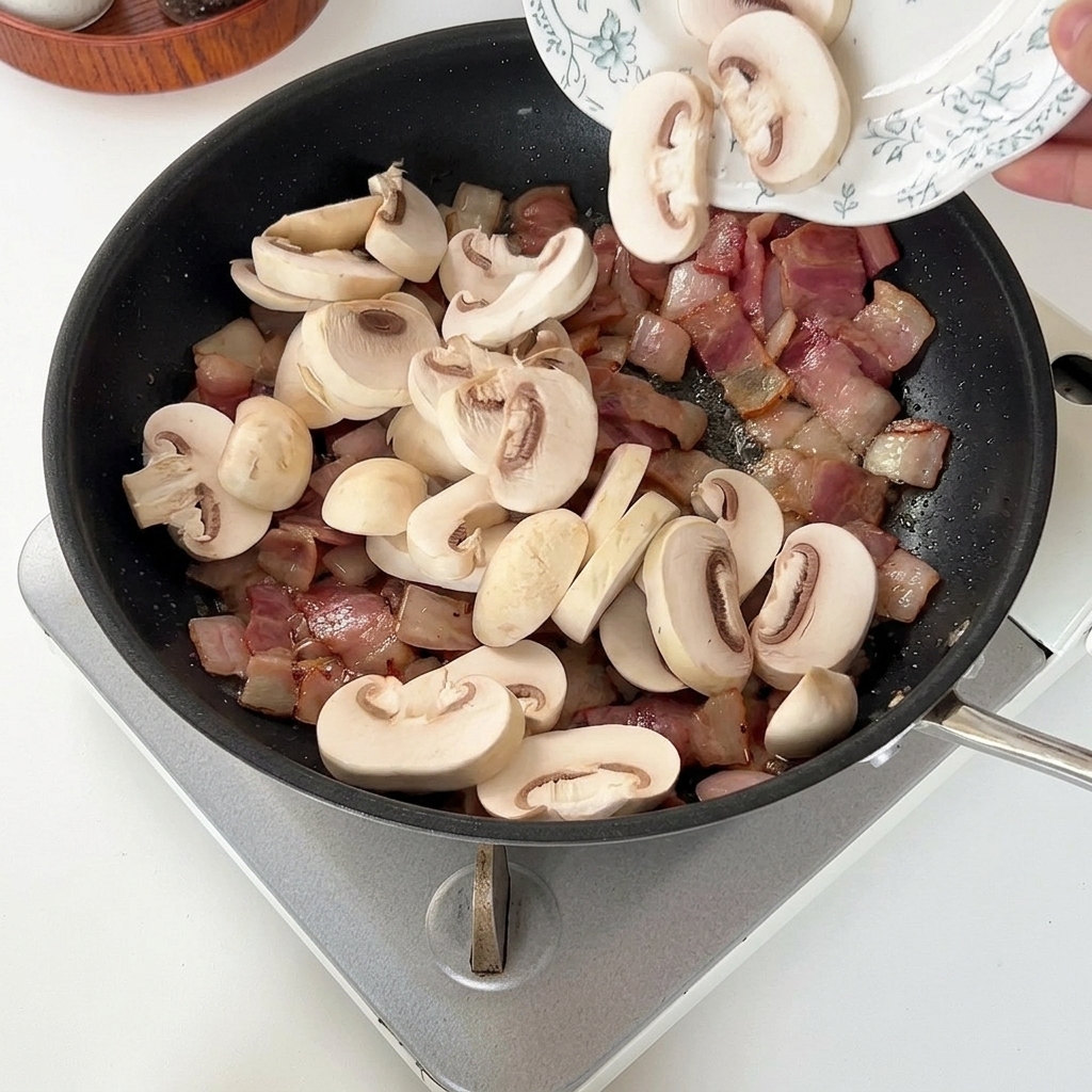 Champiñones laminados siendo añadidos a la sartén con el beicon y la cebolla.