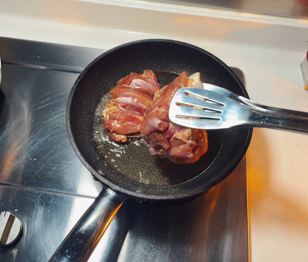 Contramuslos de pollo marinados colocándose con la piel hacia abajo en una sartén caliente con aceite brillante.