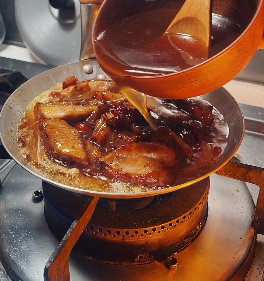 Una salsa oscura y sabrosa vertiéndose desde un cuenco naranja sobre el pollo dorado y las cebollas en la sartén.