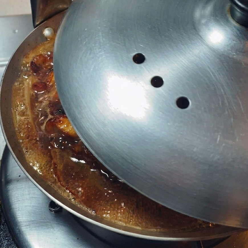 Una tapa de metal pulido colocándose sobre una sartén poco profunda para retener el vapor.
