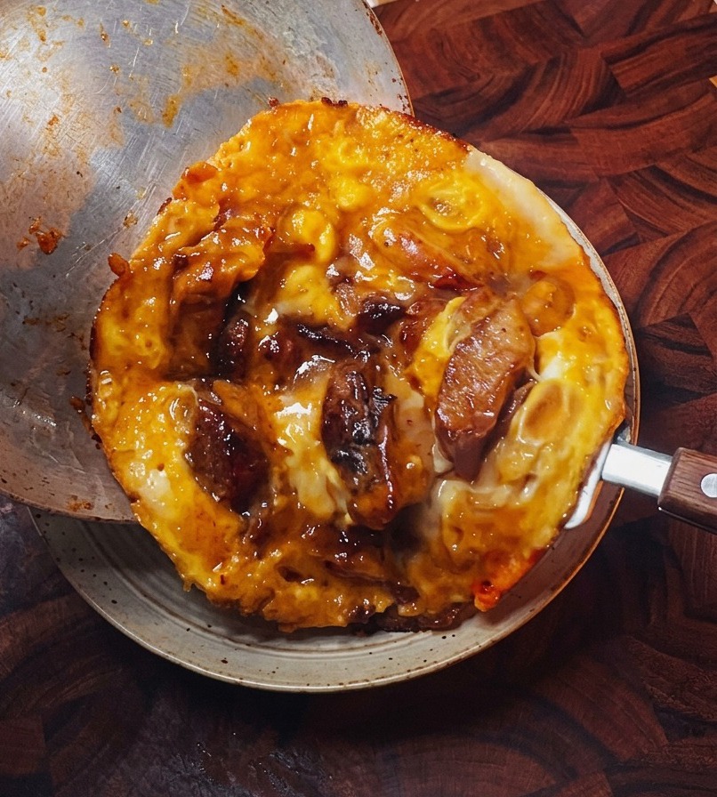 La jugosa cobertura de pollo y huevo deslizándose con delicadeza desde la sartén hacia un bol de arroz blanco esponjoso.