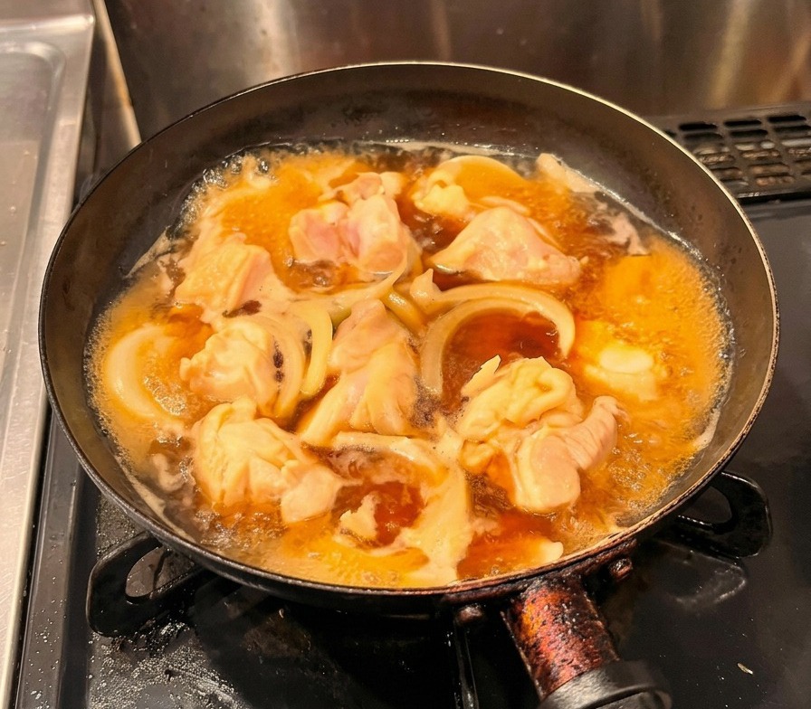 Huevos amarillos batidos vertiéndose en un flujo constante sobre el pollo y las cebollas que se cocinan a fuego lento en una sartén negra.