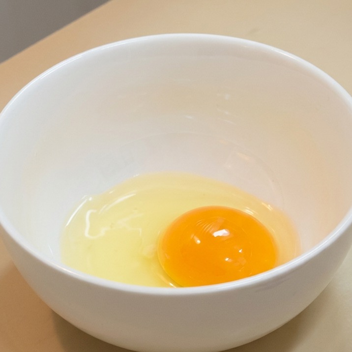 Una yema de huevo cruda y su clara translúcida reposando en un bol de cerámica blanca.
