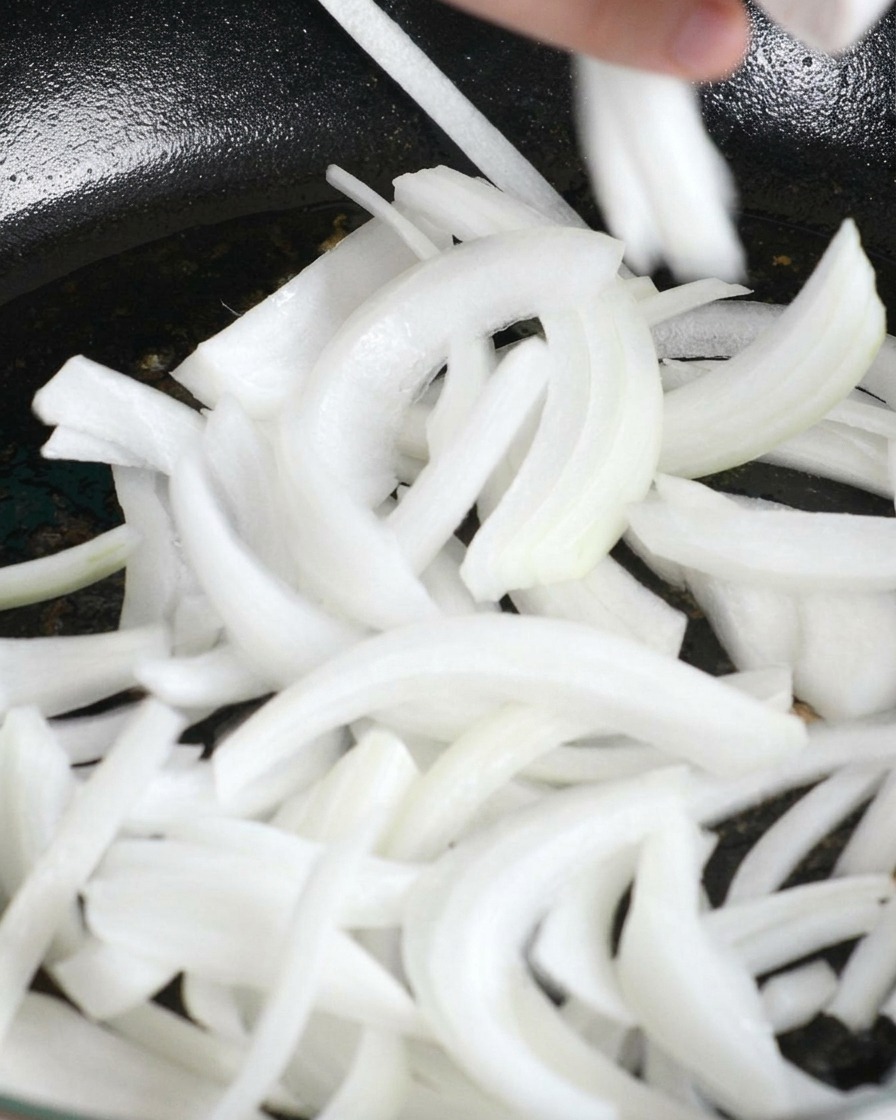 Cebollas blancas rebanadas cayendo en una sartén con la grasa derretida del pollo.
