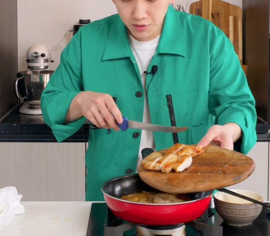 Tiras de contramuslo de pollo frito colocándose en una sartén roja que contiene cebollas a fuego lento y huevos parcialmente cocidos.