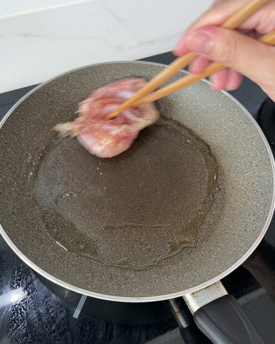 Muslos de pollo colocándose con palillos de madera en una sartén caliente con aceite, comenzando con la piel hacia abajo.