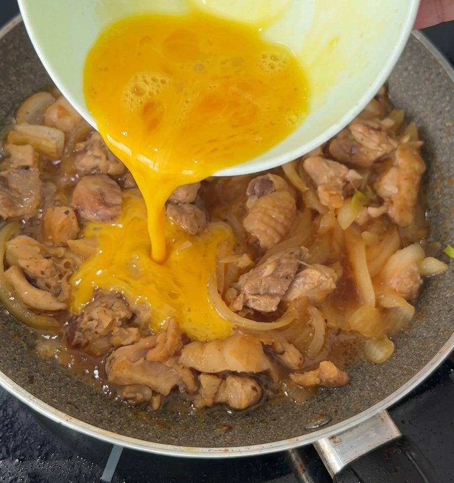 Un hilo de huevo batido vertiéndose sobre el pollo y las cebollas que hierven a fuego lento en una sartén.