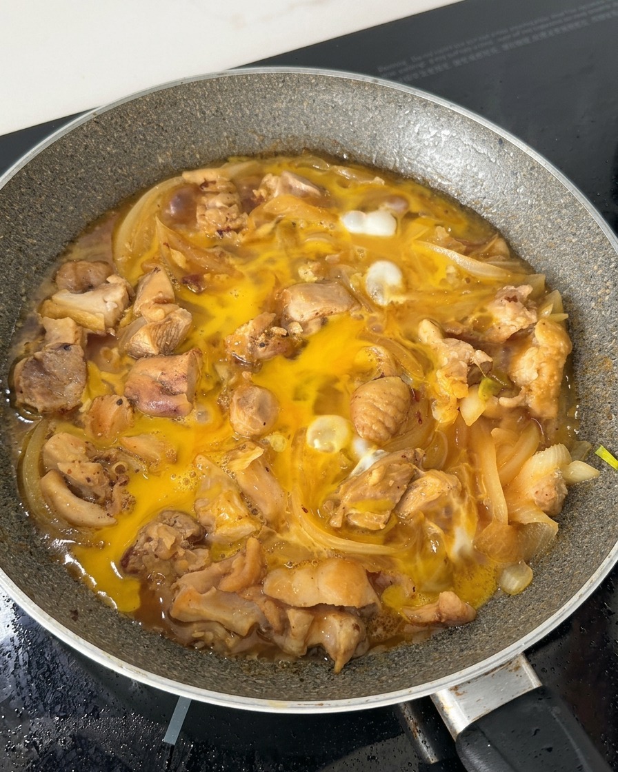 La mezcla de huevo parcialmente cocinada burbujeando en una sartén con trozos de pollo y cebolla en un caldo a base de soja.