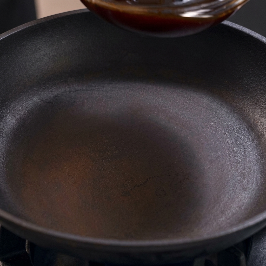 Una salsa de Oyakodon oscura y agridulce vertiéndose en una sartén negra sazonada sobre la estufa.