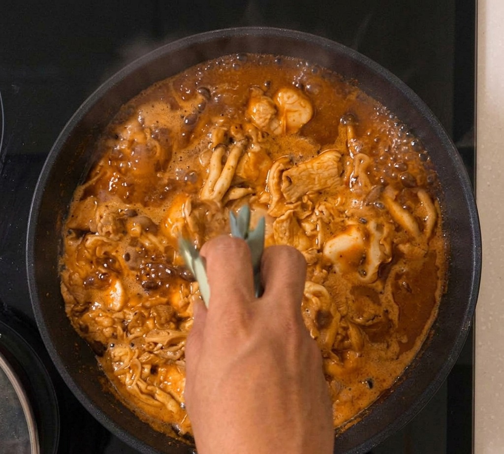 La mezcla de Oyakodon burbujeando en una sartén con cebolleta visible entre el huevo que cuaja y el pollo.
