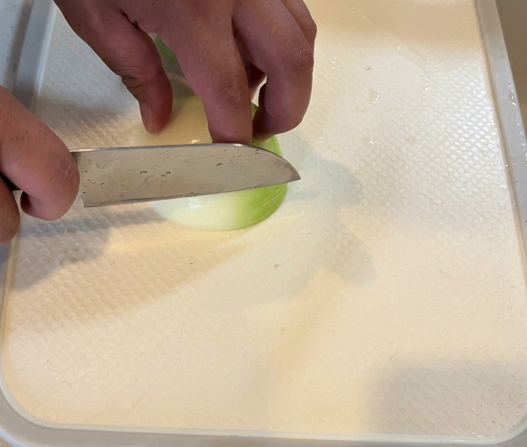 Una persona cortando una cebolla blanca en gajos finos sobre una tabla de cortar blanca.