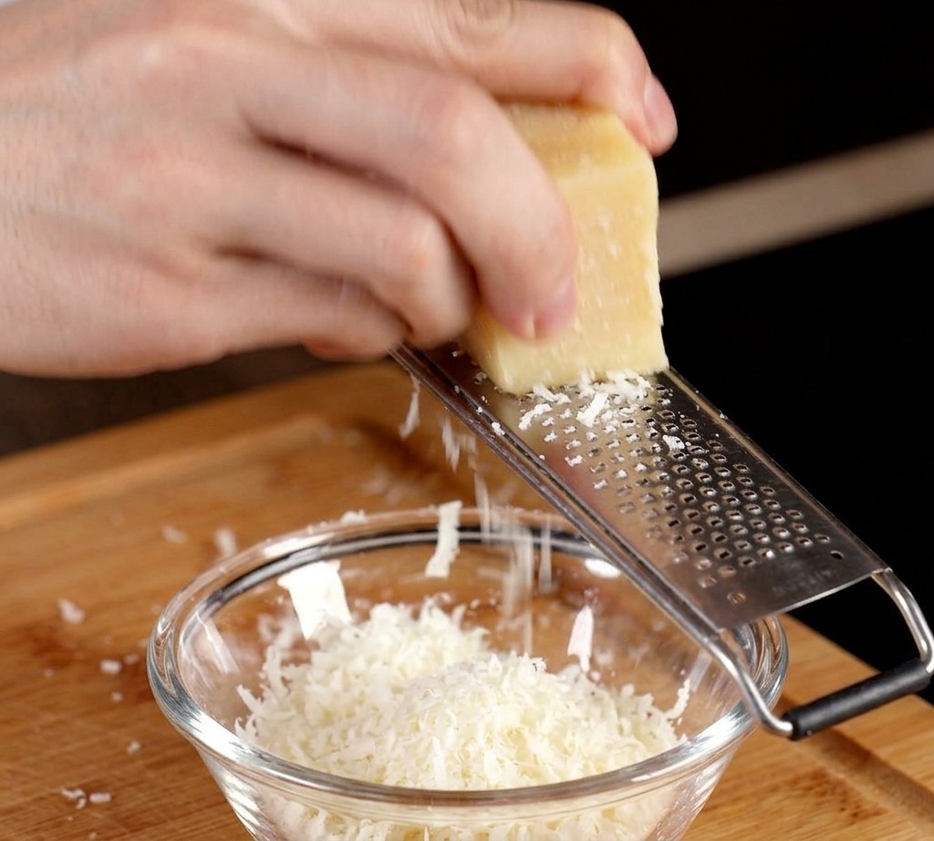 Rallando un bloque de queso parmesano en un bol pequeño con una yema de huevo cruda.