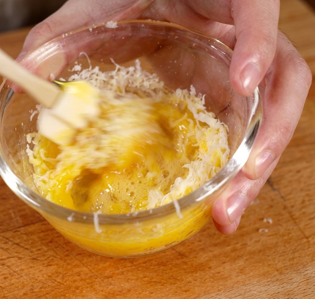 Batiendo la yema de huevo y el queso rallado en un bol de vidrio para formar una pasta amarilla espesa.