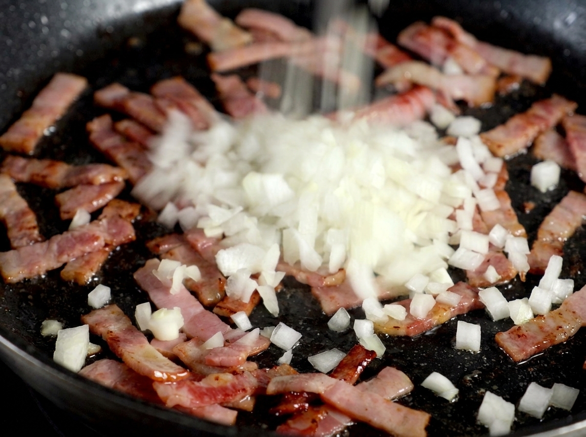 Cebolla blanca picada siendo esparcida sobre una sartén con tiras de bacon crujiente.