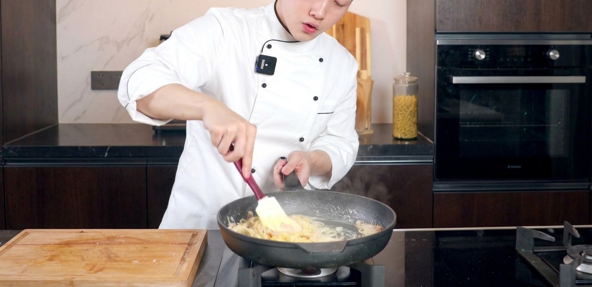 Chef removiendo pasta cremosa en una sartén con una espátula para integrar la salsa.