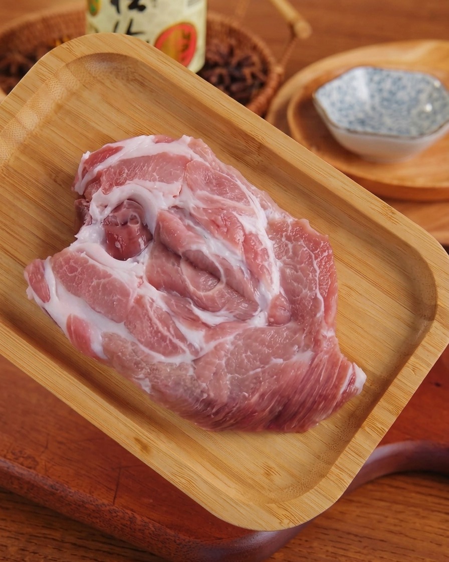 Una pieza aplanar de cerdo veteado crudo sobre una bandeja de madera después de ser espalmada.
