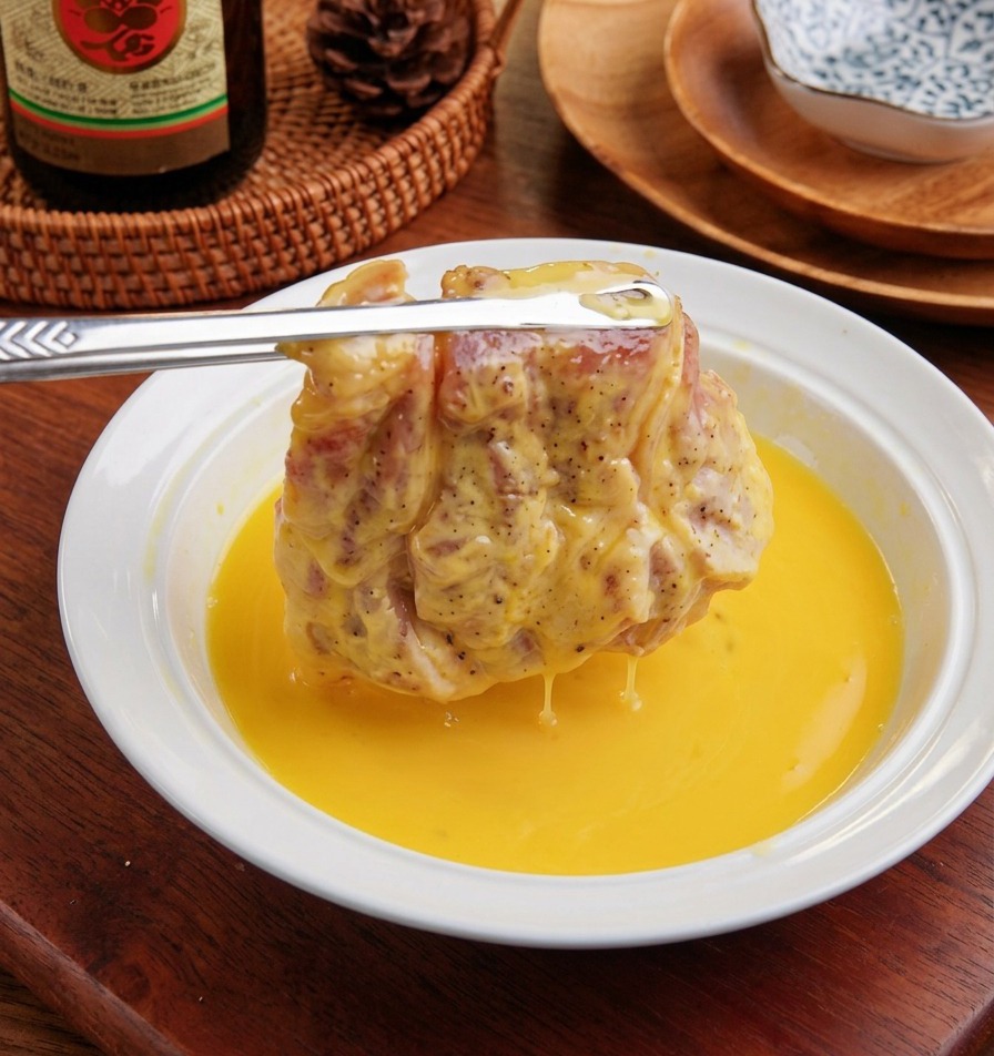 Una chuleta de cerdo enharinada sumergiéndose en un tazón blanco con huevo batido.