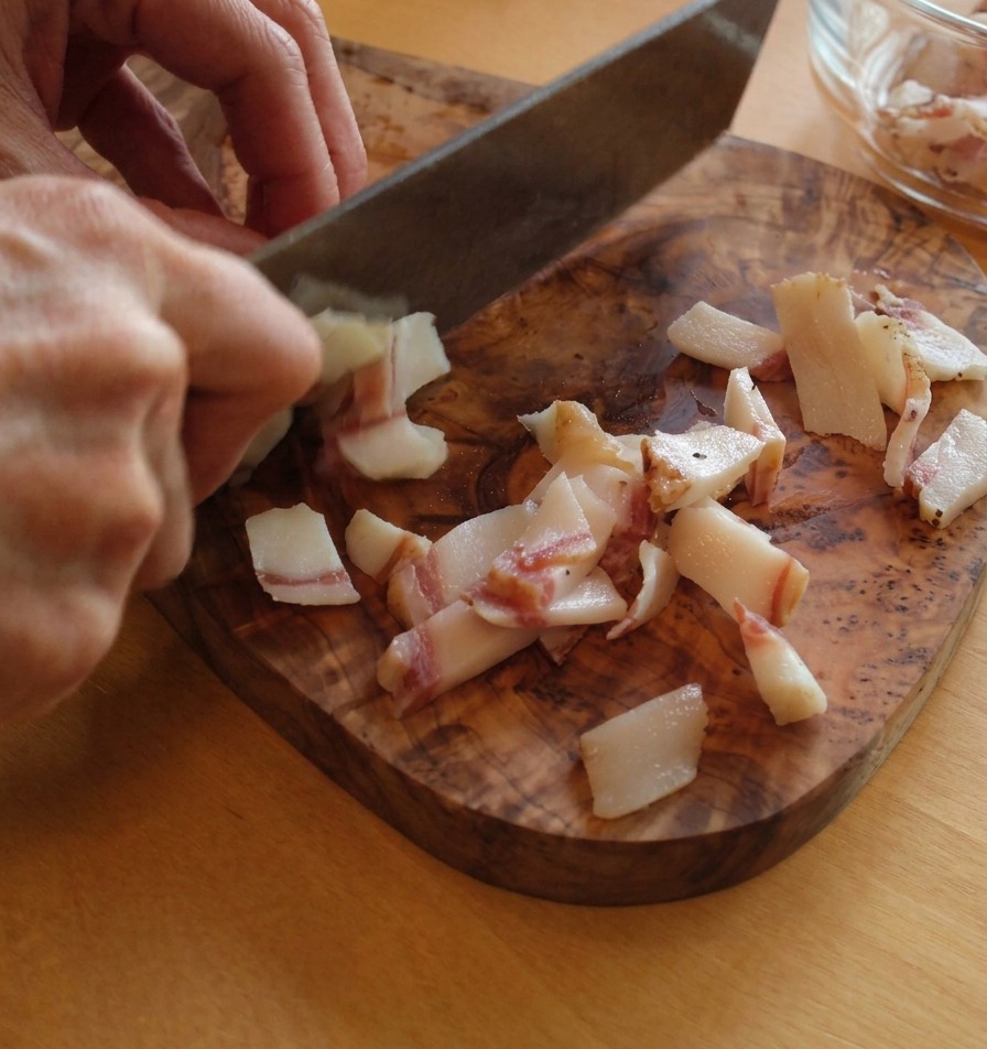 Cortando guanciale en pequeñas tiras rectangulares sobre una tabla de cortar, mostrando las capas de grasa y carne.