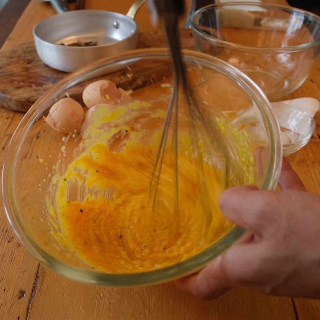 Mezclando yemas de huevo y queso en un bol mientras se añade un chorrito de agua caliente de la pasta.