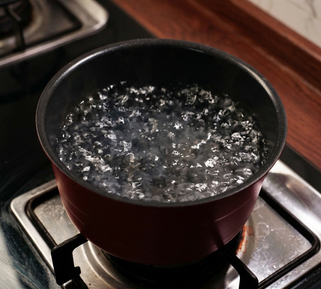 Una olla de color rojo oscuro sobre un fogón de gas con agua hirviendo y vapor subiendo.