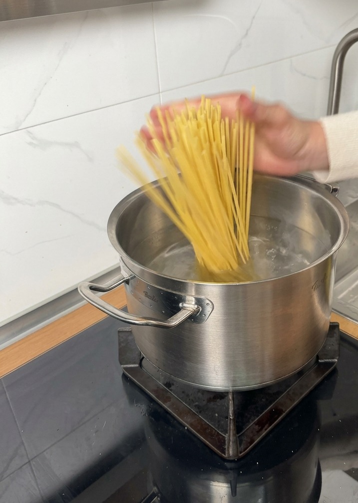 Pasta seca introduciéndose en una olla de agua hirviendo en una placa de inducción.
