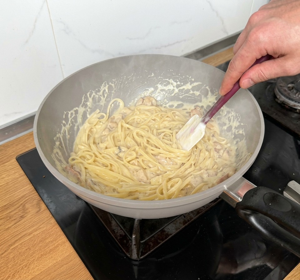 Mezclando los linguine en una sartén con salsa rica, tiras de beicon y champiñones troceados.
