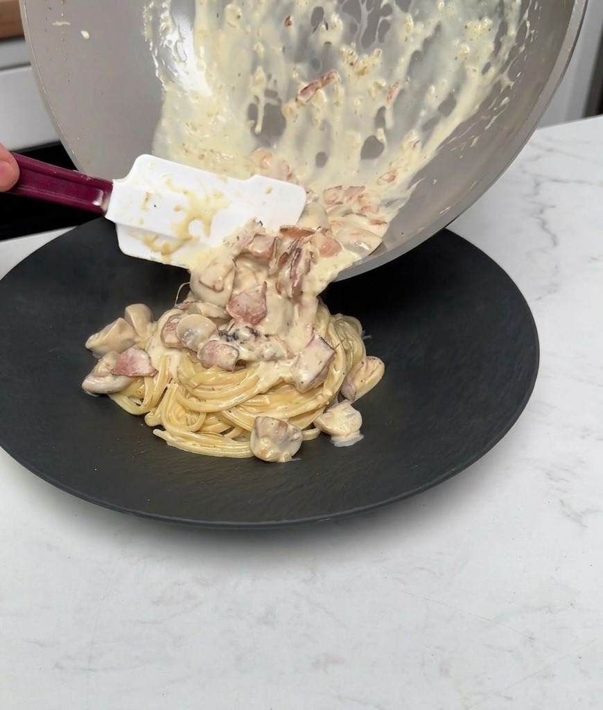 Vertiendo el resto de la salsa cremosa con champiñones y beicon sobre la pasta ya emplatada.