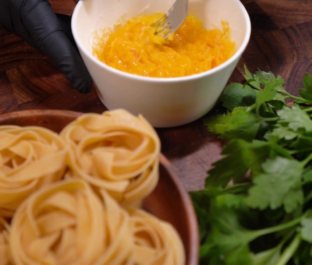 Una persona batiendo las yemas de huevo y el queso rallado con un tenedor en un tazón blanco para crear la base de la salsa.