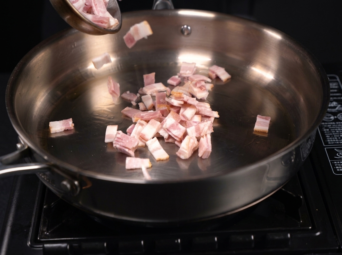 Pequeños trozos de tocino picado chisporroteando y soltando su grasa en una sartén de acero inoxidable.