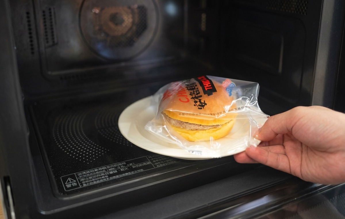 Una mano colocando la parte superior de un pan brioche tostado sobre la hamburguesa con cebolla y queso.