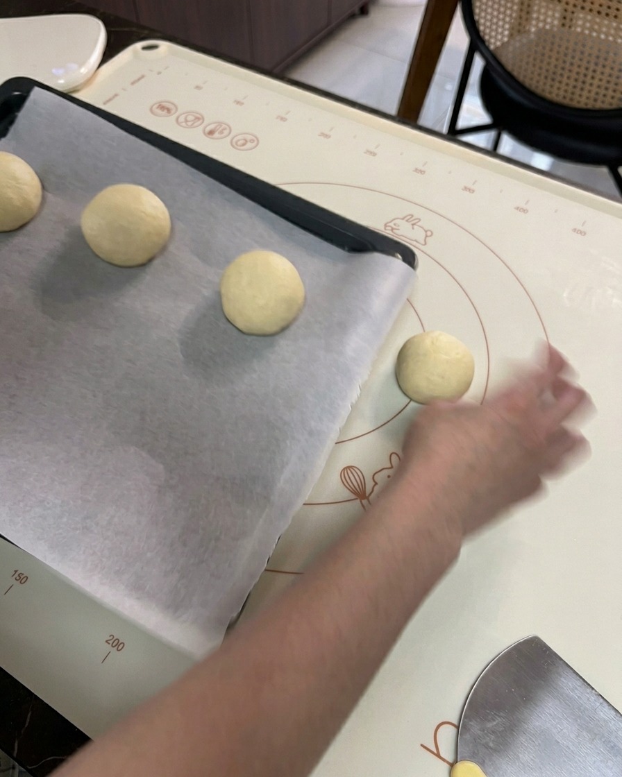 Una mano colocando las bolas de masa ya formadas en una bandeja de horno negra forrada con papel vegetal.