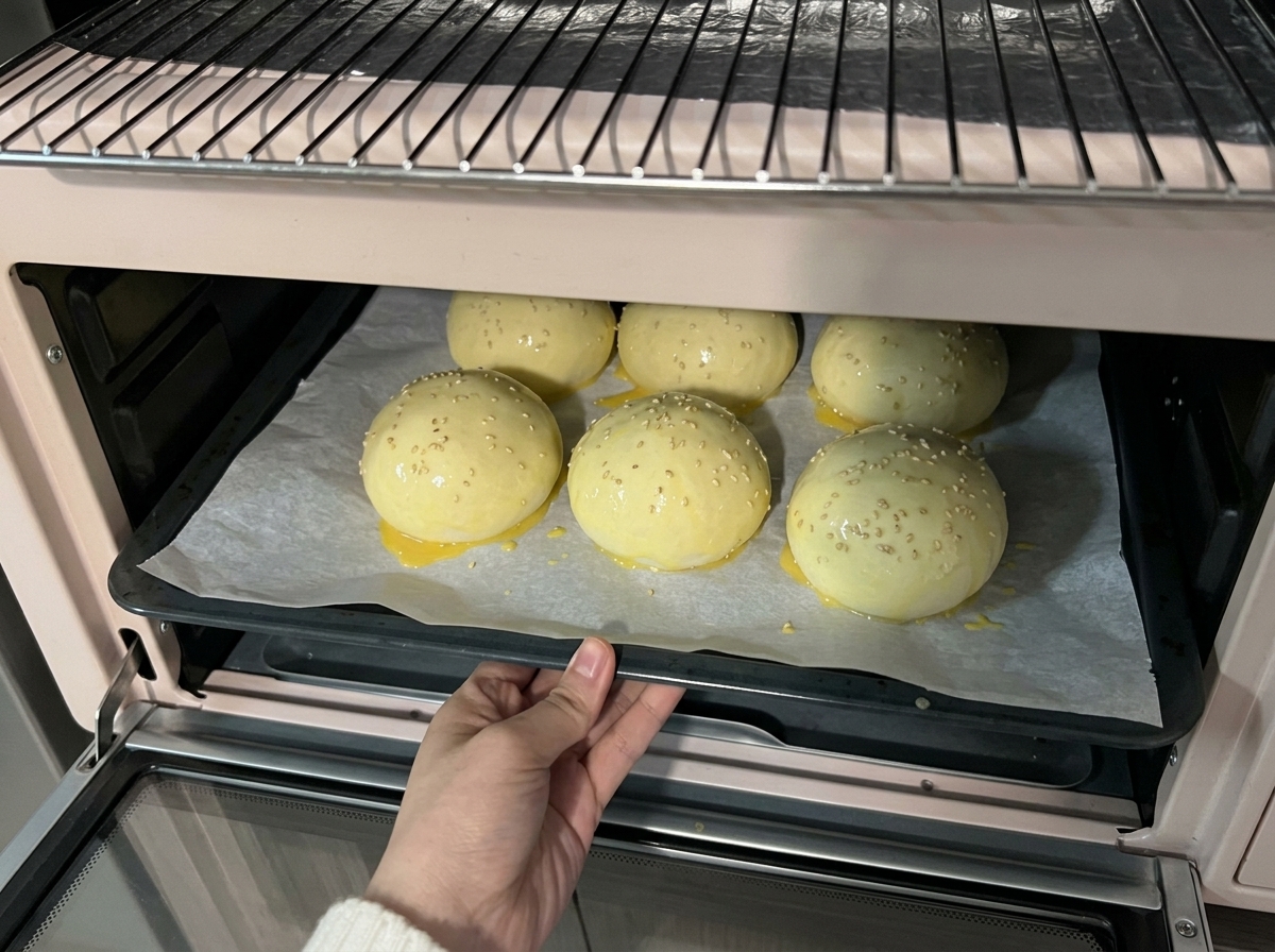 Una bandeja con las bolas de masa cubiertas de sésamo entrando en un horno de sobremesa de color rosa claro.