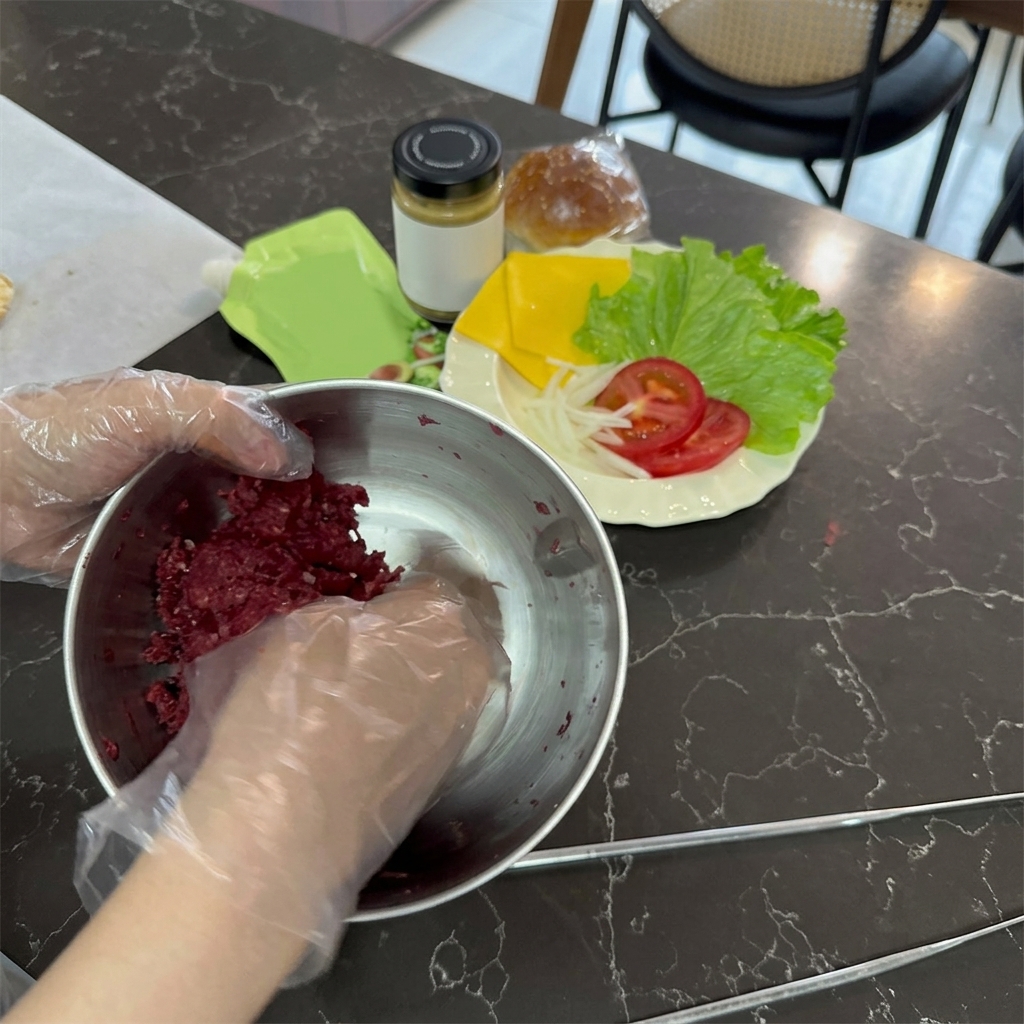 Manos con guantes de plástico transparente mezclando carne picada de ternera cruda en un bol de acero inoxidable.