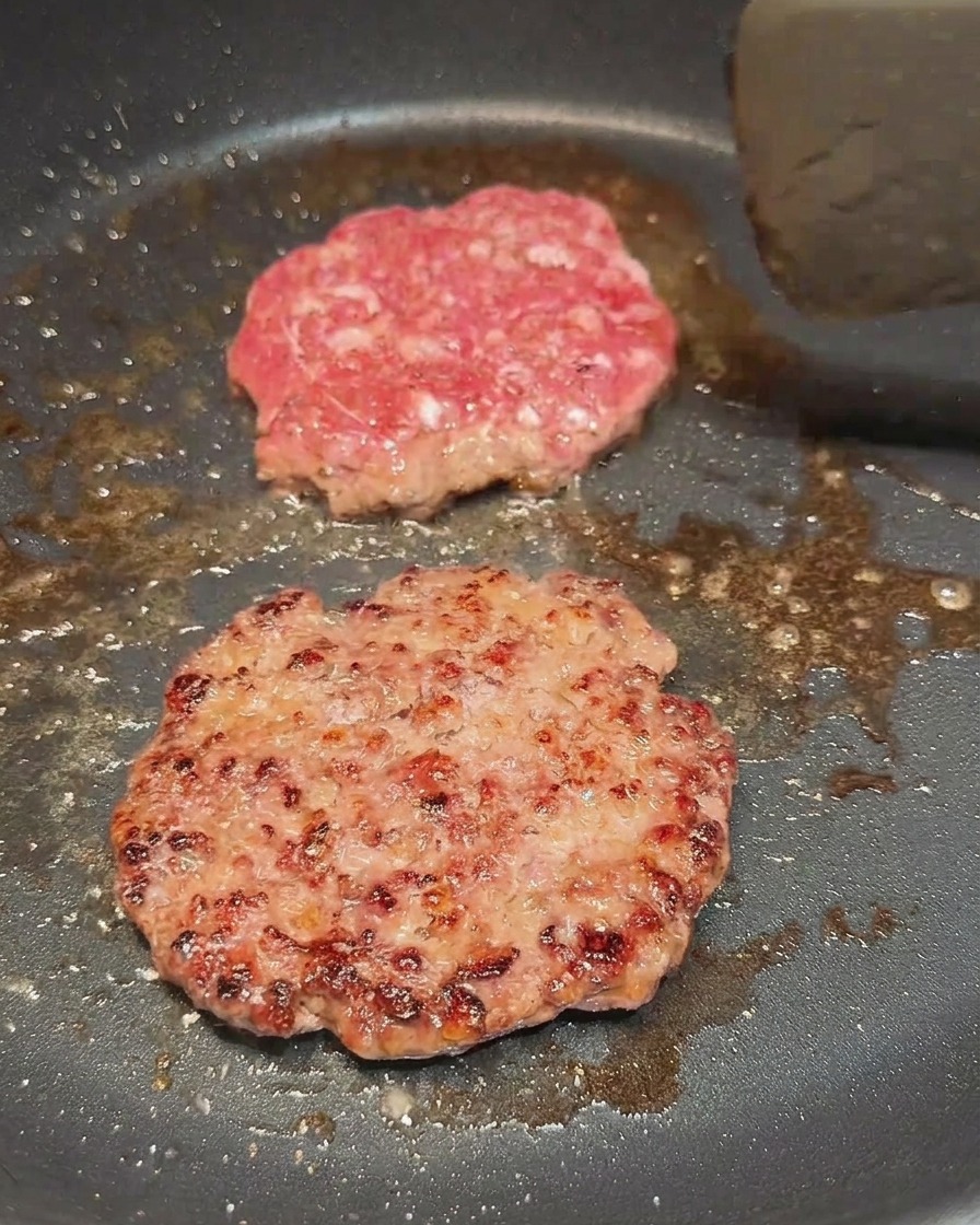 Dos carnes cocinándose, una recién volteada mostrando una costra dorada y oscura.