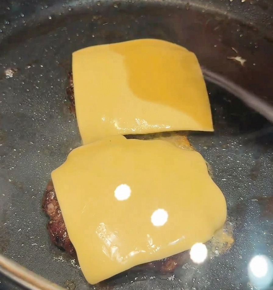 Dos rebanadas de queso sobre dos carnes selladas en una sartén negra.