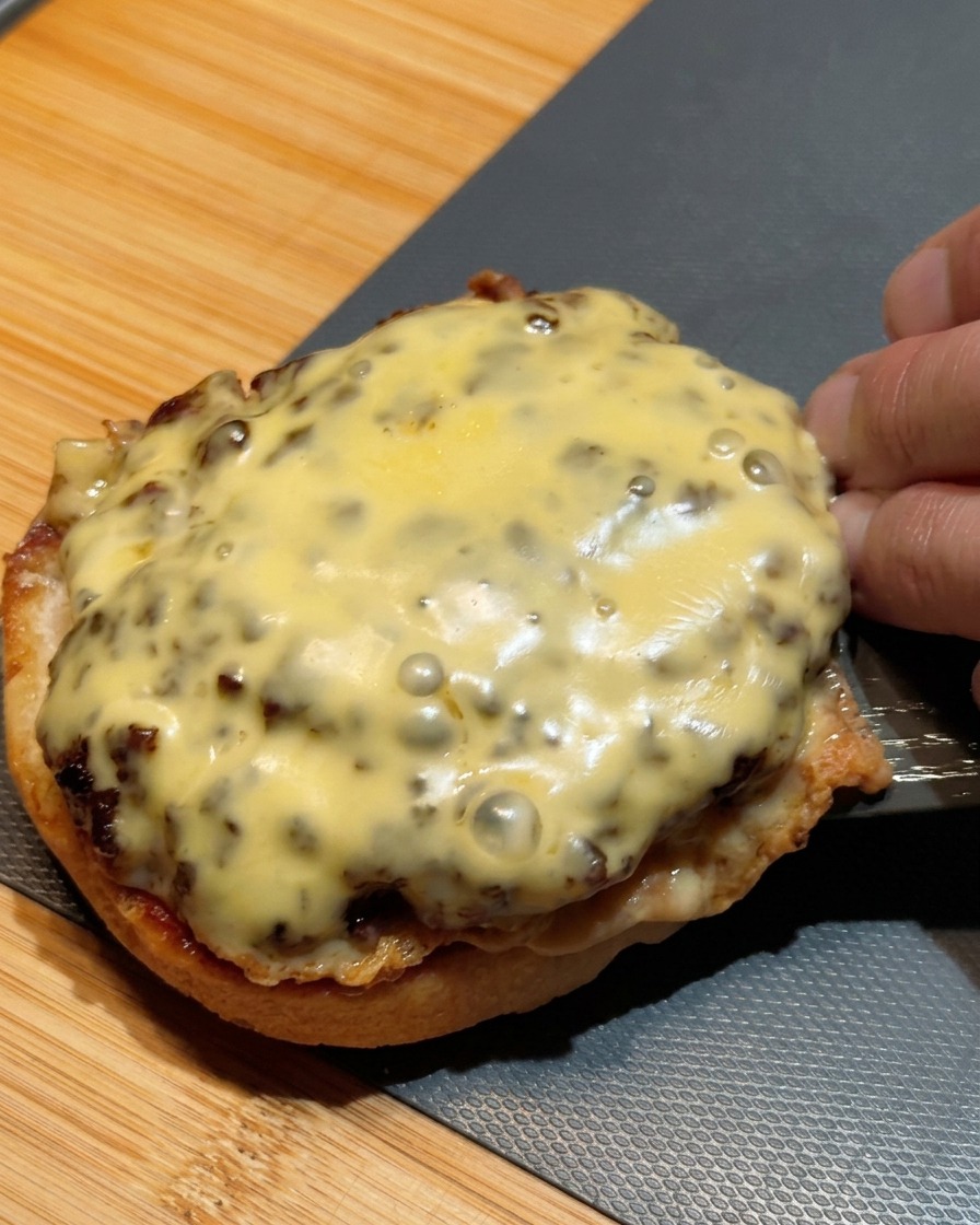 Una espátula transfiriendo dos carnes apiladas y cubiertas de queso derretido hacia el pan base.