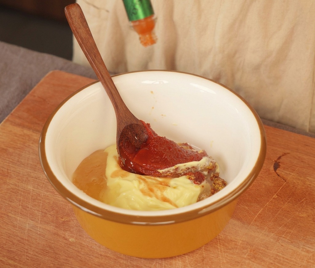 Salsa picante siendo añadida a un bol con mayonesa y mostaza.
