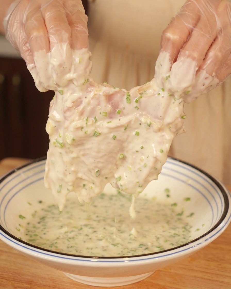 Manos levantando un contramuslo de pollo cubierto con una masa espesa llena de cebollino.