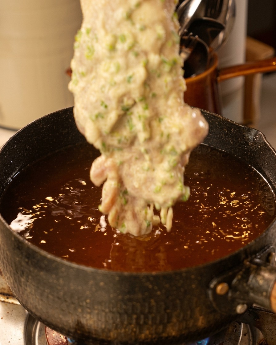 Bajando un contramuslo rebozado a una olla con aceite caliente burbujeante.