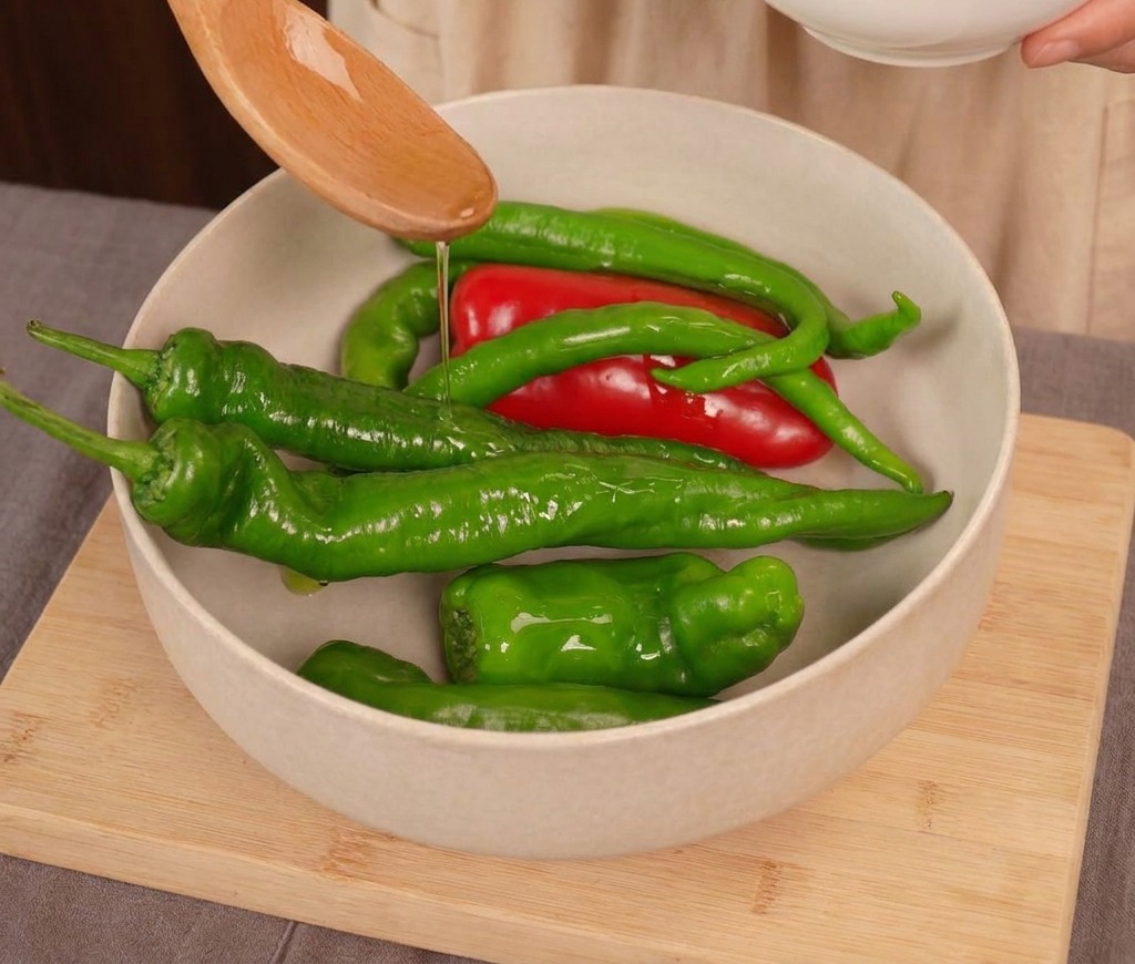 Aceite de cocina vertiéndose sobre una mezcla de chiles rojos y verdes frescos en un bol claro.