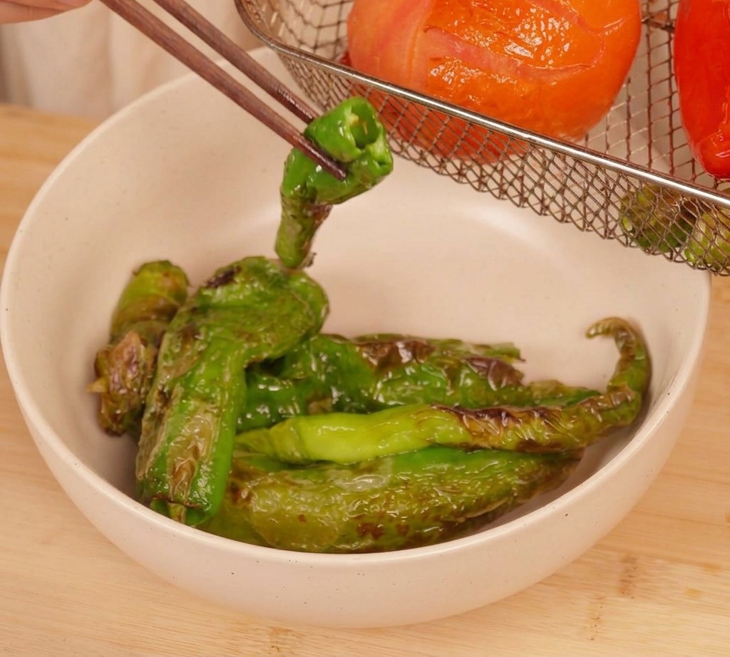 Palillos levantando un chile verde asado de la cesta de la freidora de aire con el tomate ya blando.