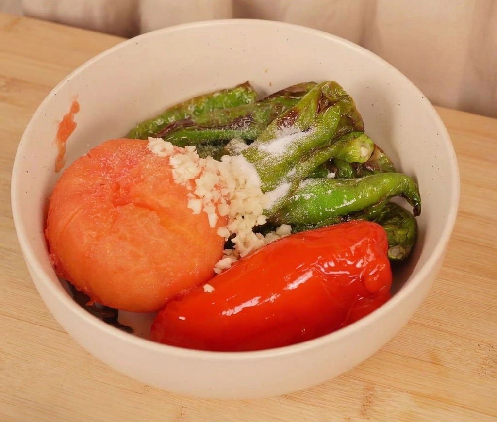 Un bol con chiles y tomate asados cubiertos con ajo picado y sal antes de mezclarse.