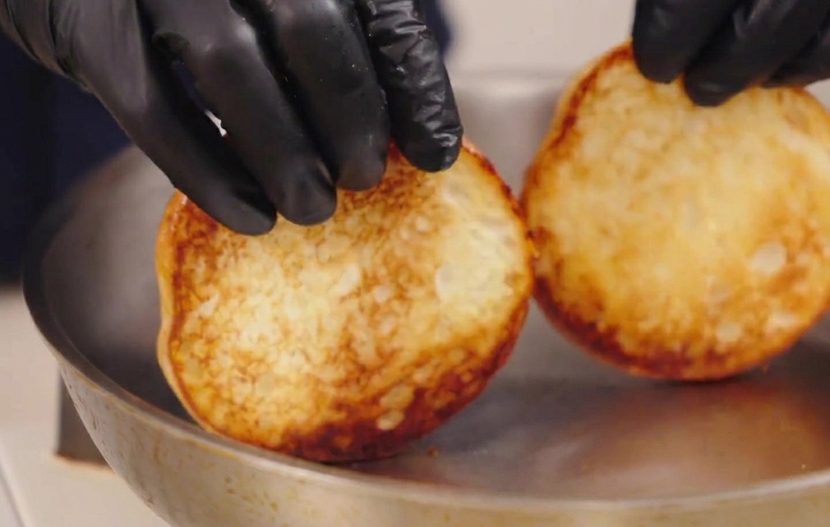 Manos levantando dos panes tostados de una sartén, mostrando sus bases perfectamente doradas.