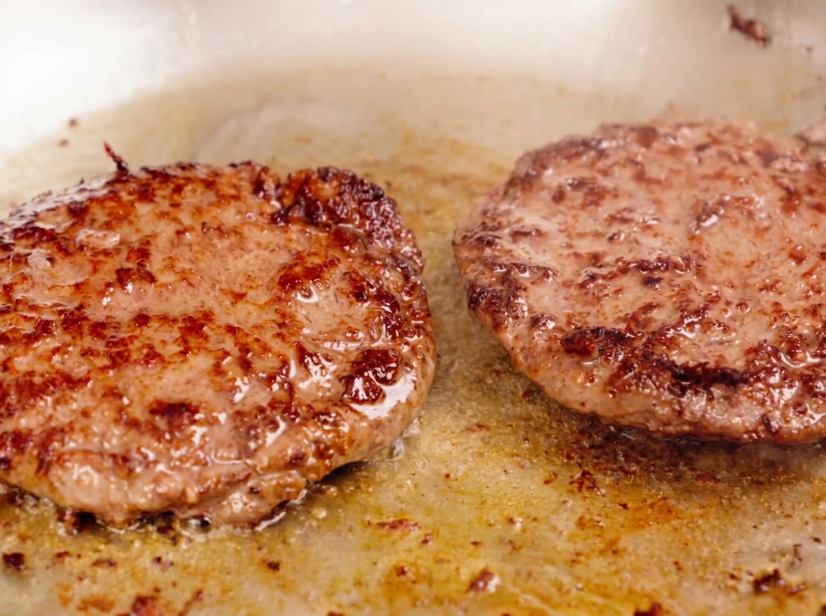 Dos piezas gruesas de carne sellándose en una sartén, con una costra dorada y jugos burbujeando en la superficie.