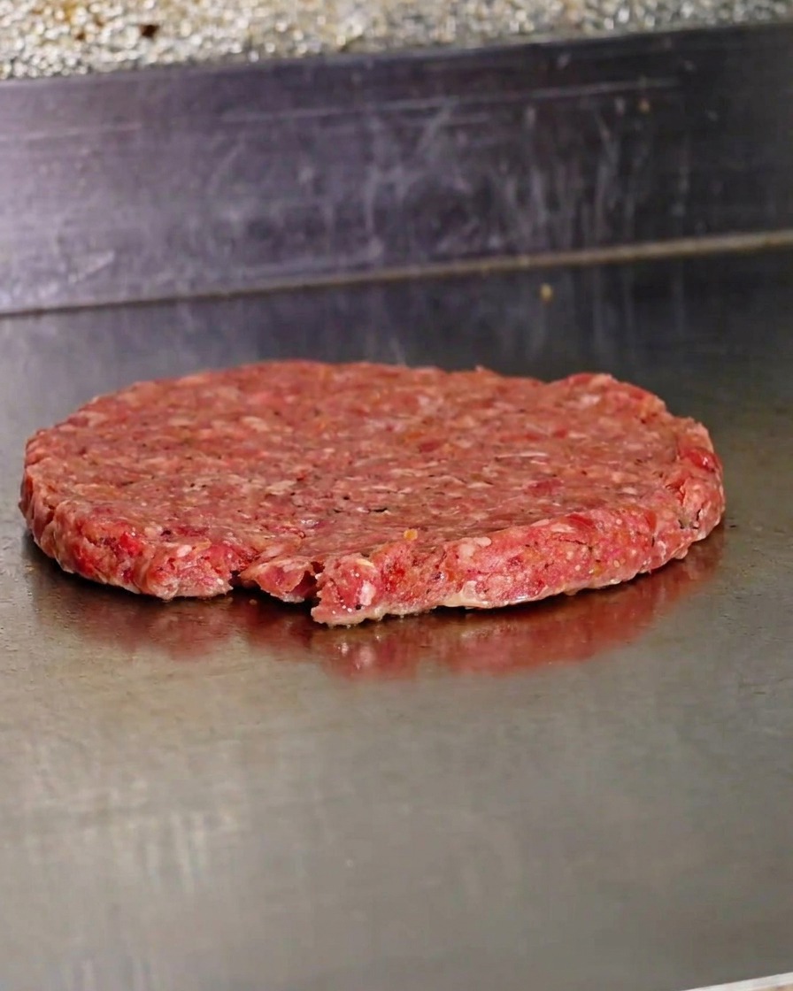 Una hamburguesa recién aplastada cocinándose en una plancha de metal caliente.