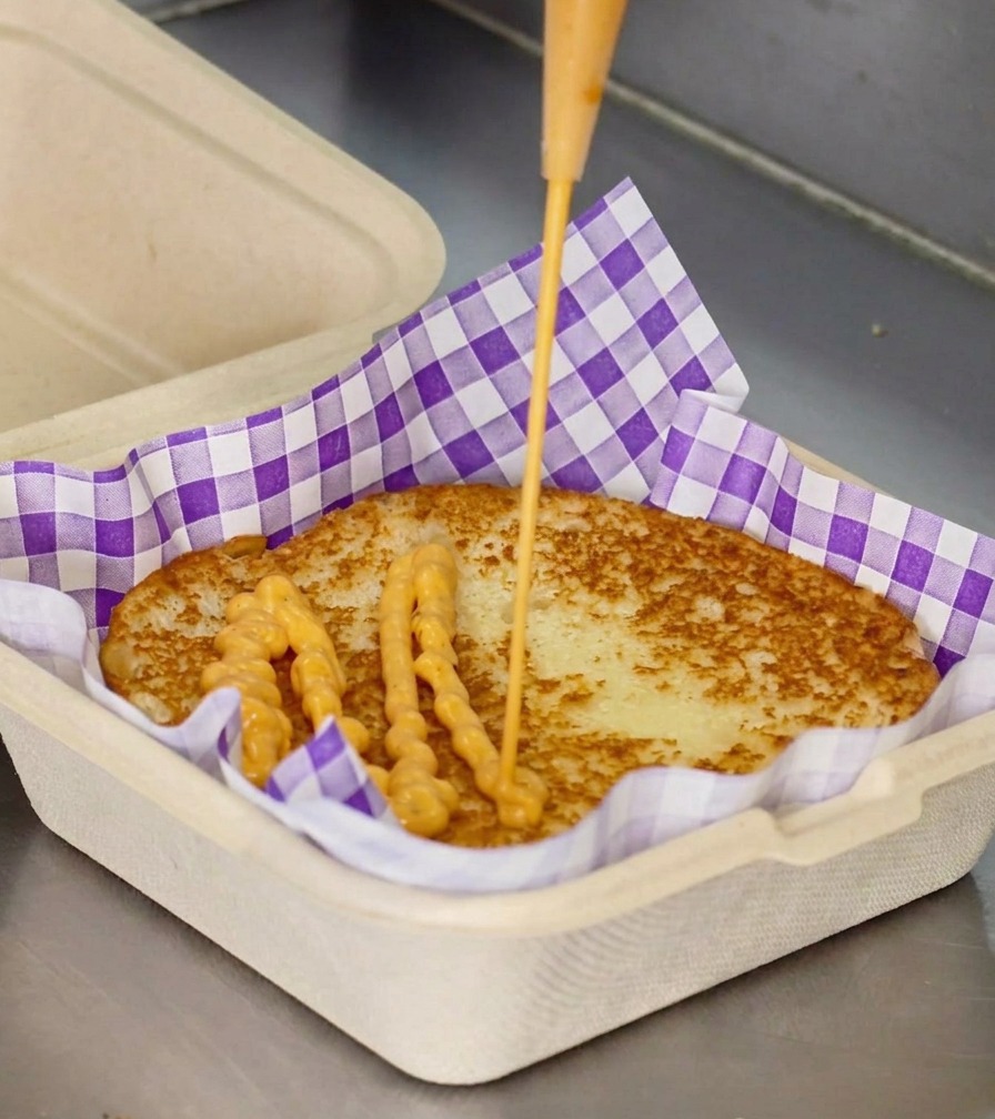 Salsa cremosa de color naranja cayendo desde un biberón sobre el pan tostado en una caja con papel de cuadros.