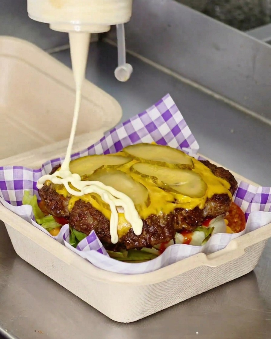 Mayonesa blanca cayendo en zigzag sobre la hamburguesa con queso.
